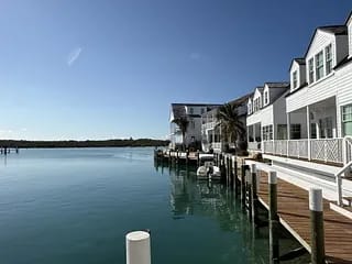 Exterior front view with dock, boats, white buildings, palm trees, and calm water.
