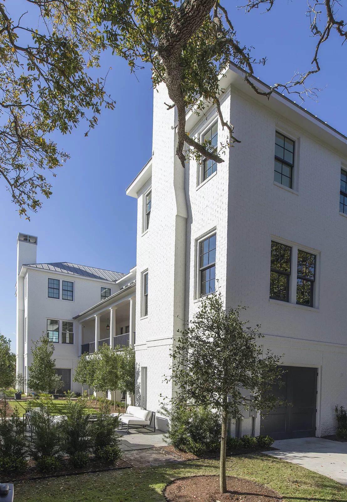 Front exterior of a two-story white brick house with large windows and landscaped yard.