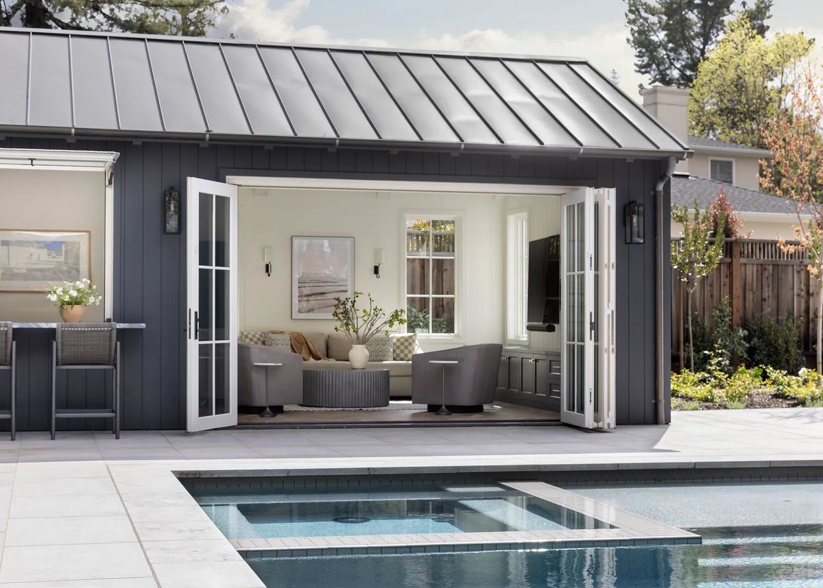 Outdoor structure with open doors, armchairs, coffee table, and pool view.