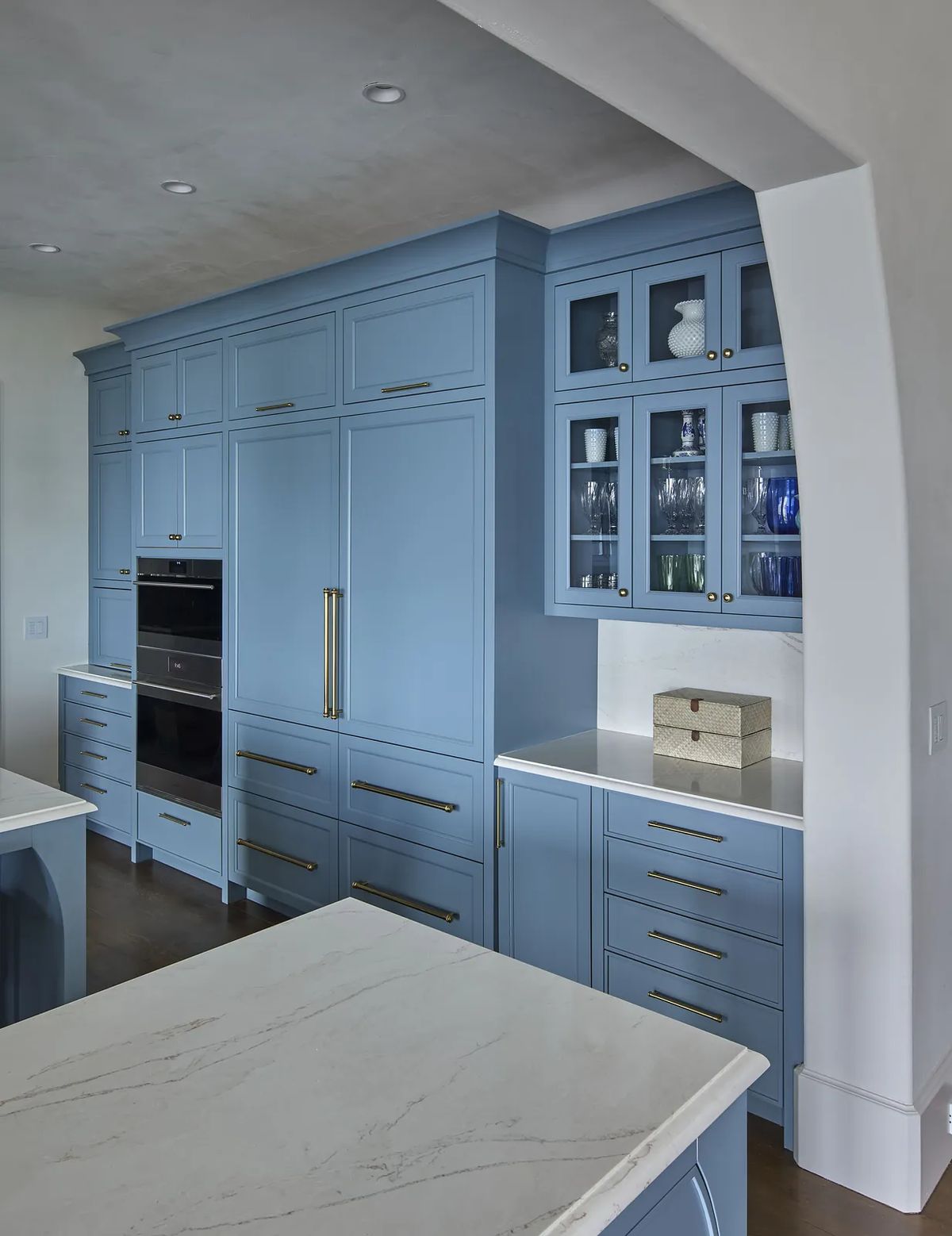 Kitchen with blue cabinetry, marble countertop, and glass-front cabinetry displaying dishware