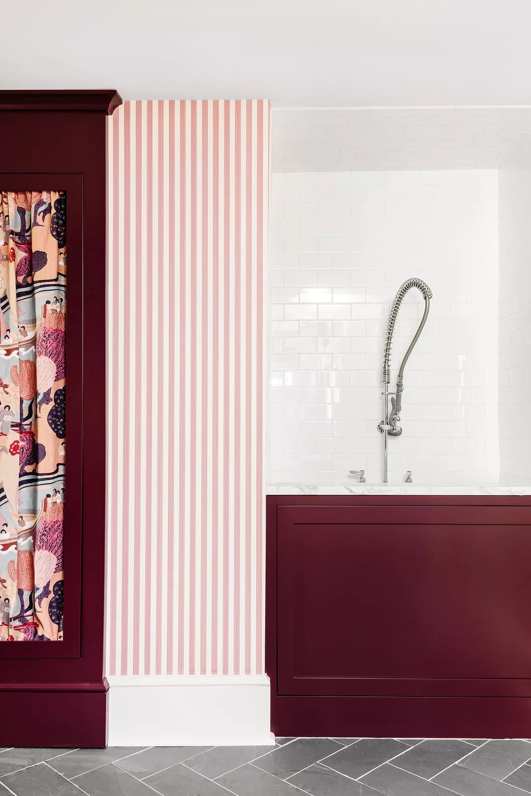 Laundry room with burgundy cabinets, dog bath, pink striped wallpaper, and white subway tile.