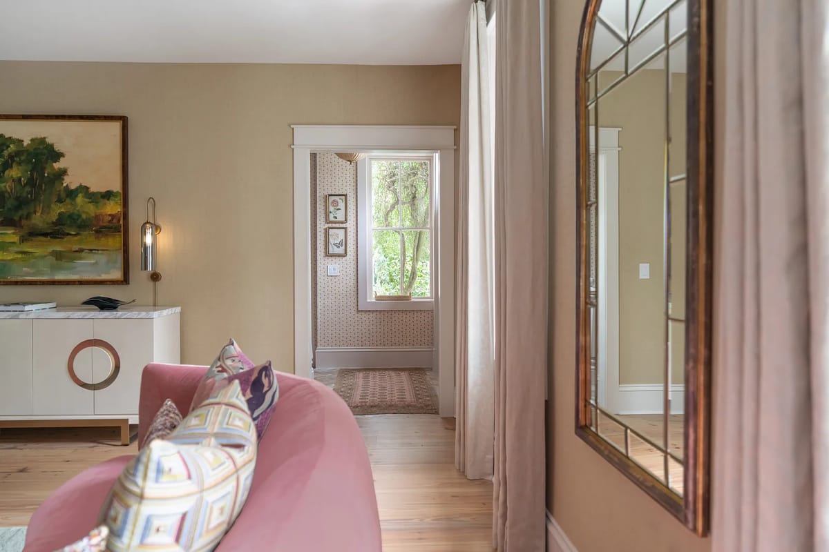 Living room with pink sofa, marble side table, large painting, decorative pillows, and natural light from a window.
