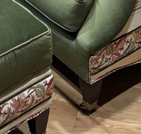 Close-up view of green upholstered chairs with floral trim and wooden legs on light wood floor.