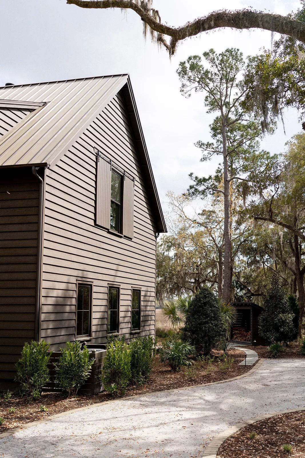 Exterior view of a house with brown siding, metal roof, windows, and landscaped front yard with gravel pathway.