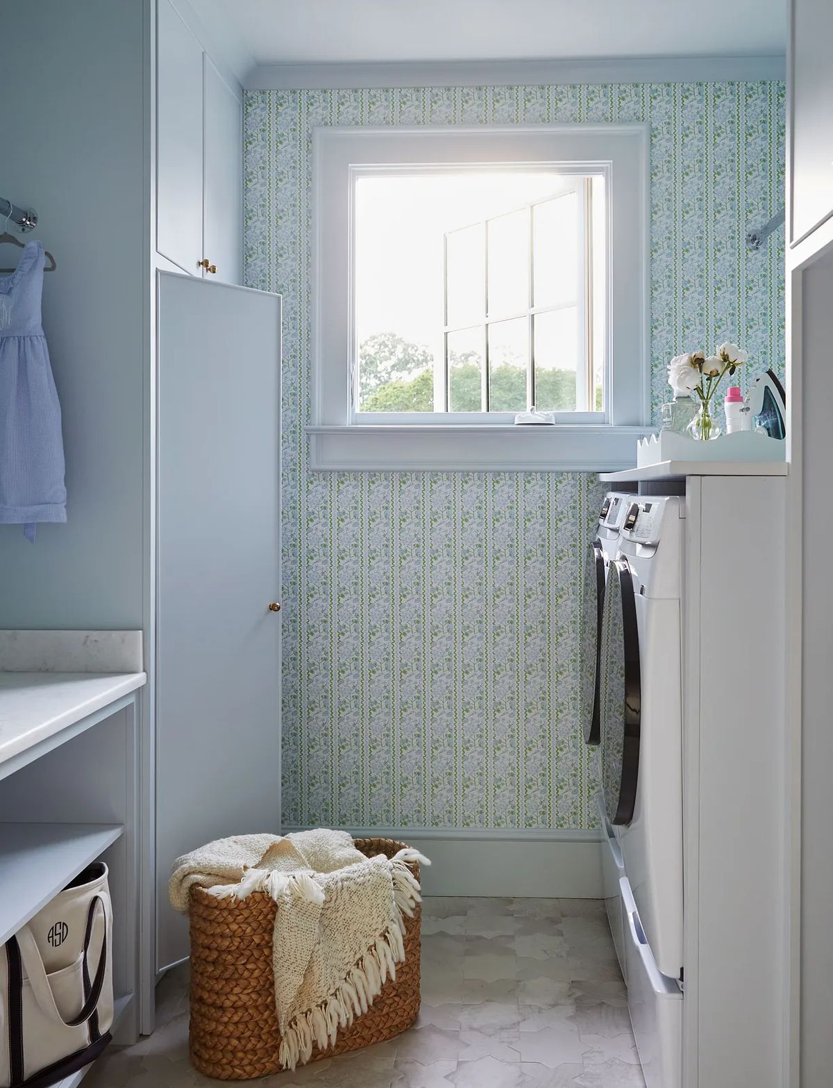 Laundry room with washer, dryer, marble countertop, patterned wallpaper, window, and woven basket.