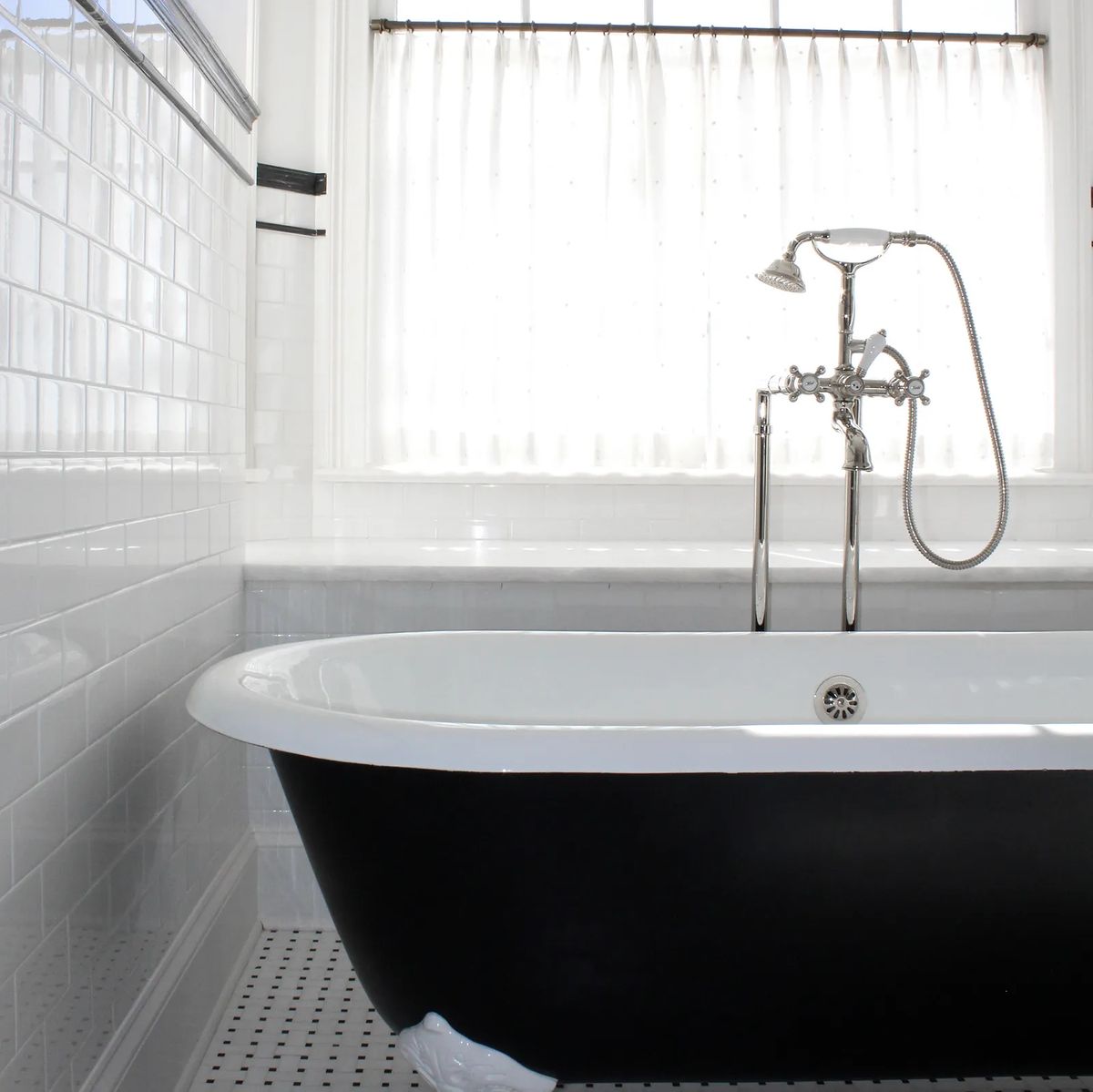 Bathroom with freestanding black and white bathtub, tiled walls, and a shower fixture with natural light from a window