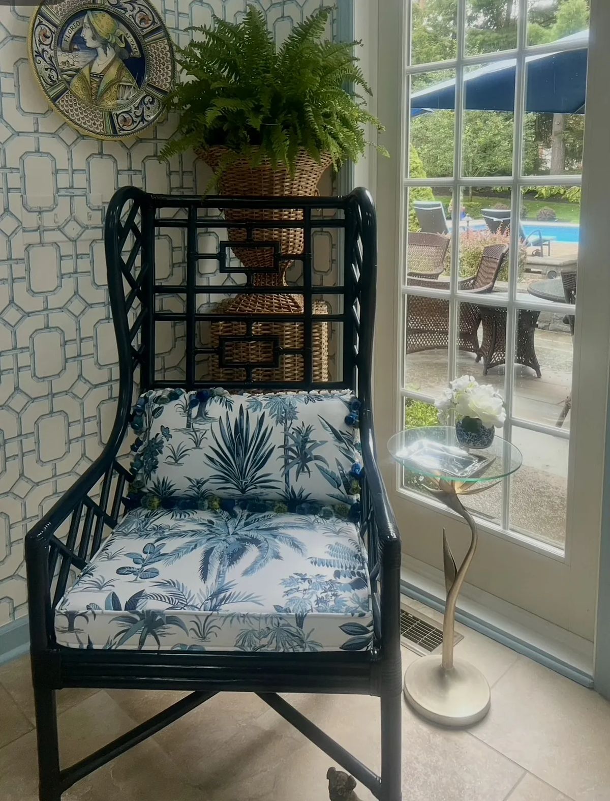 Seating area with black wicker chair, floral cushion, small glass side table, and a view of the pool.