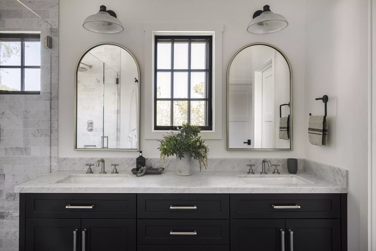 Bathroom with double vanity, black cabinet, white marble countertop, two mirrors, and textured tile work.