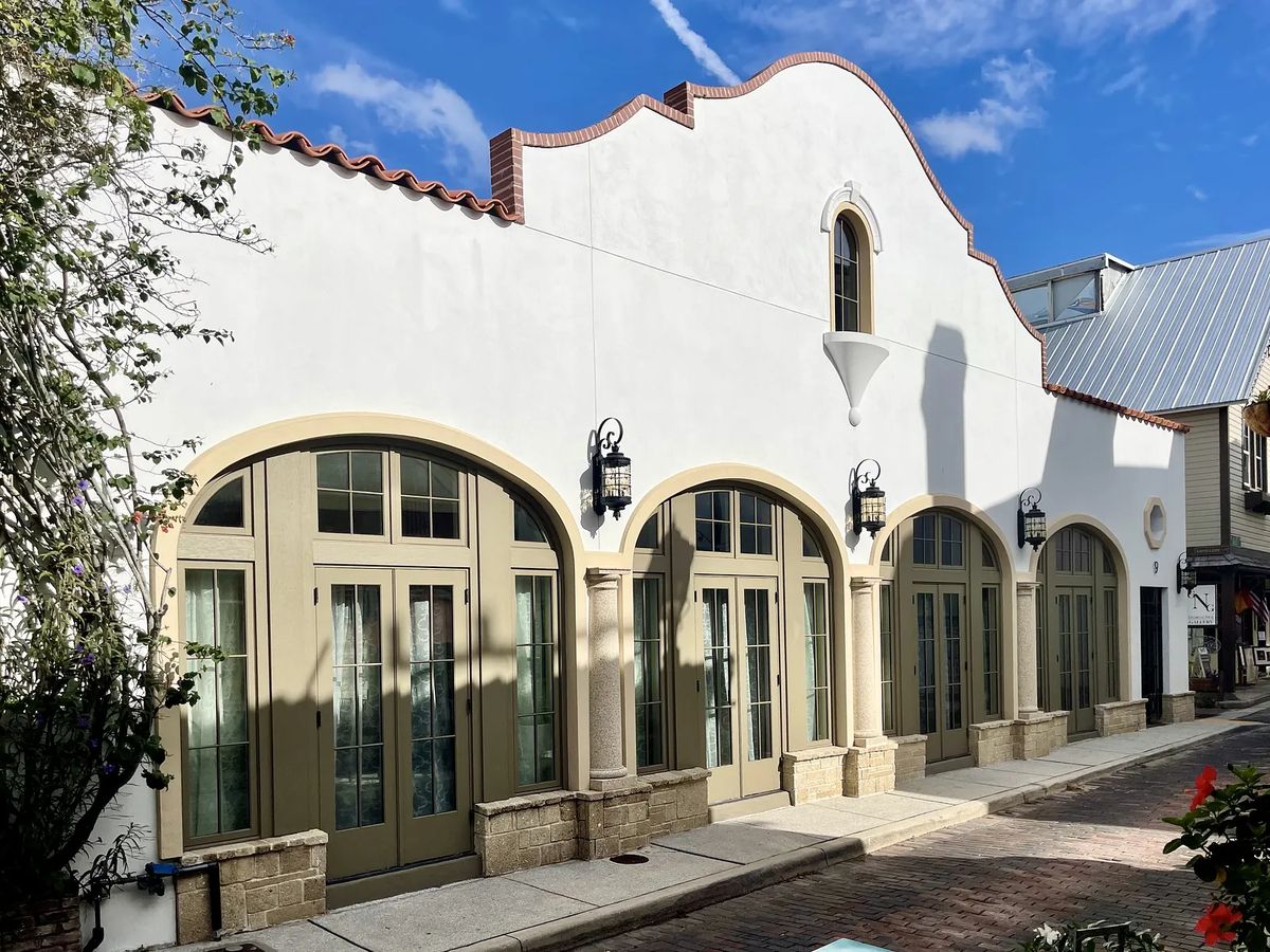 Exterior facade with white stucco, arched windows, beige frames, red-tiled roof, and wall sconces.