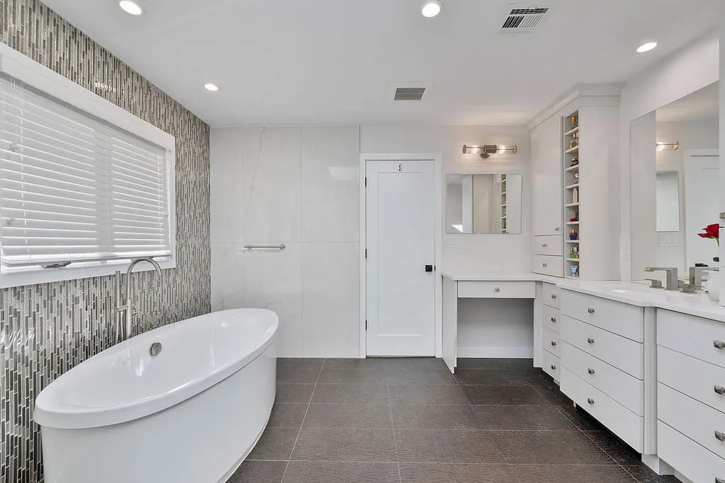 Bathroom with freestanding oval bathtub, white vanity, mosaic backsplash, and gray tiled flooring.