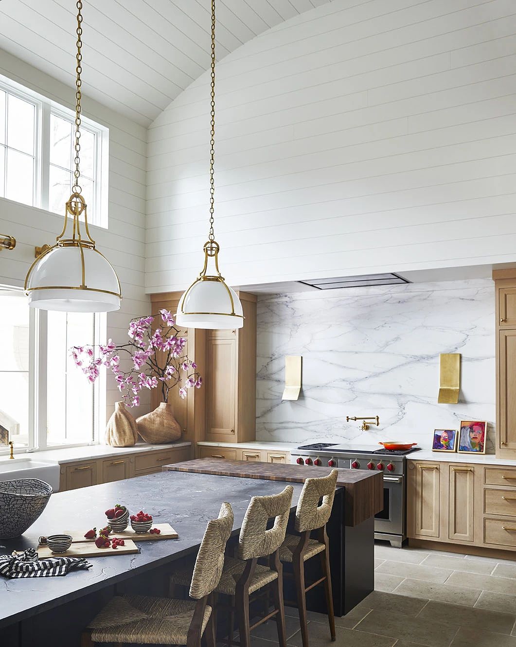Kitchen with central island, white cabinetry, marble countertop, and large windows with flowering branch.