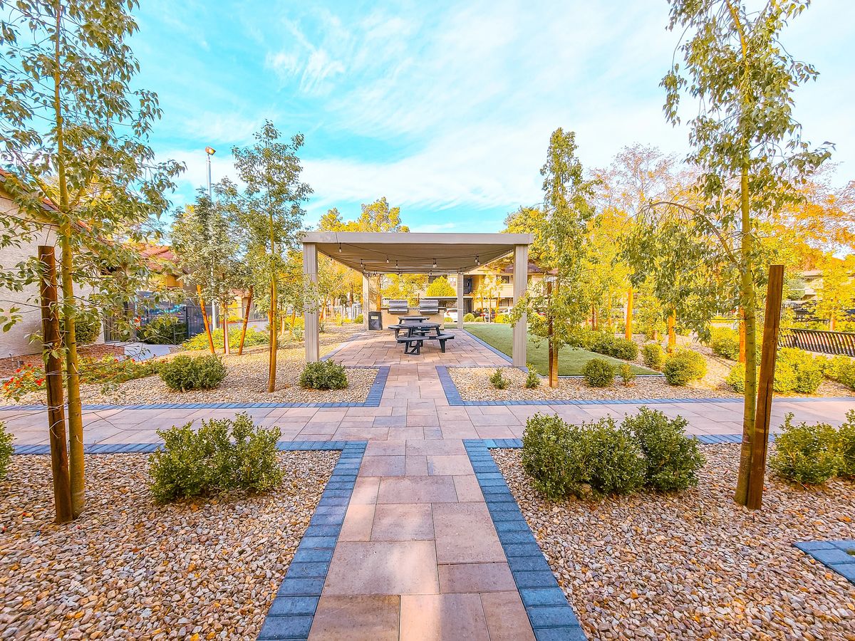 Garden area with stone pathway, shrubs, trees, covered seating with benches, and a picnic table.