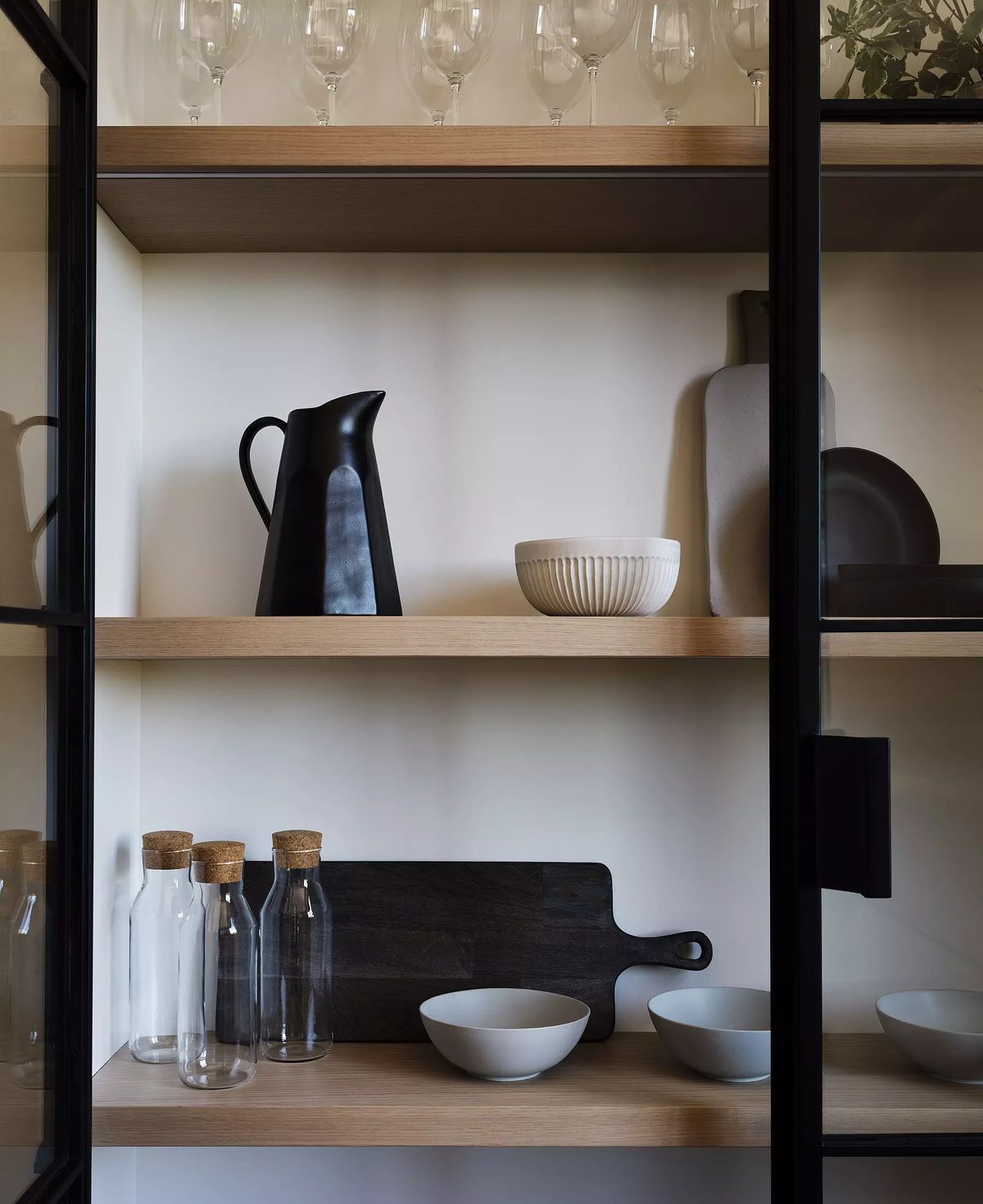 Butler's pantry with open shelving displaying glassware, ceramics, and wood cutting board.