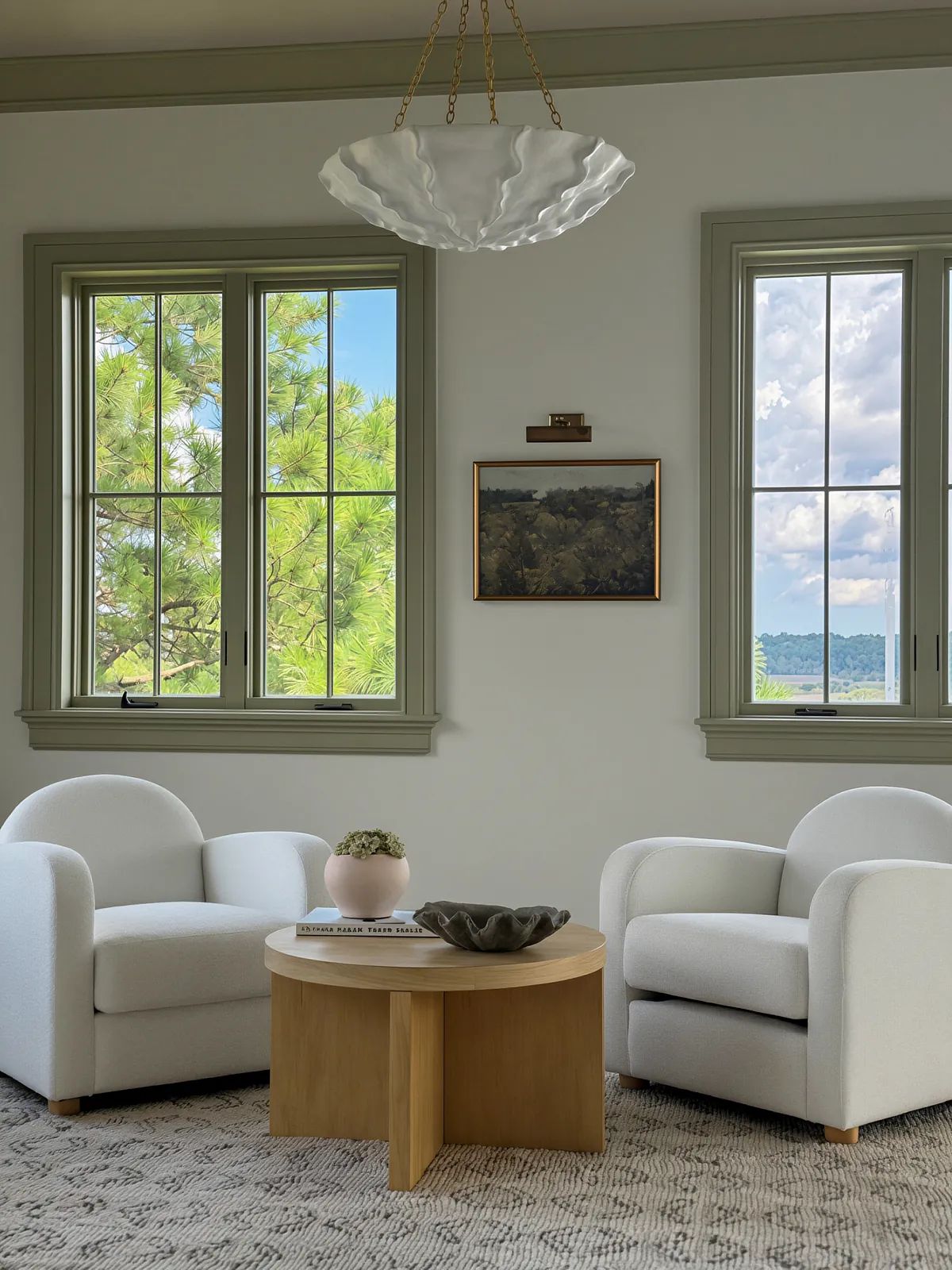 Living room with white armchairs, round wooden coffee table, area rug, and large windows with scenic view.