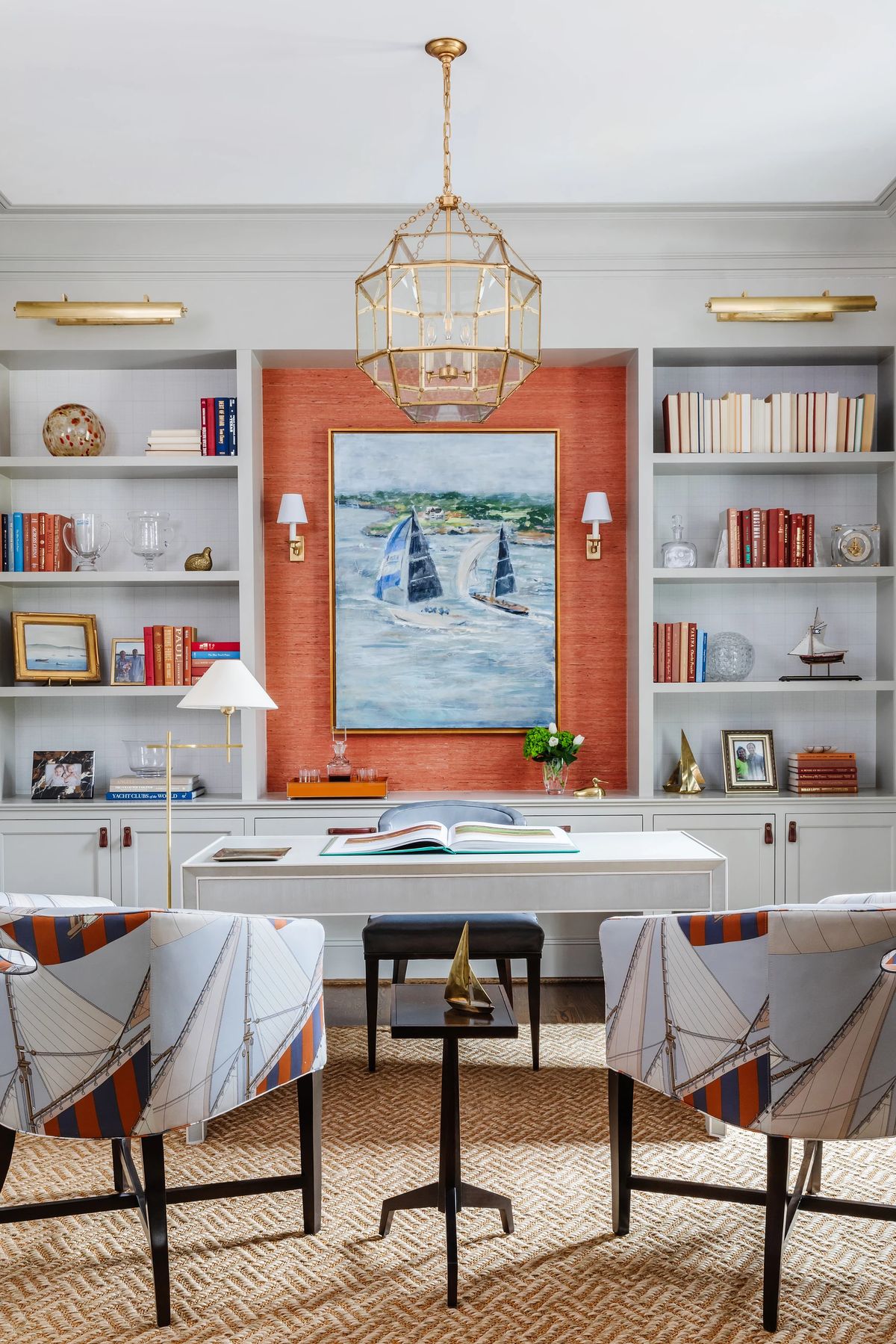 Office with white desk, patterned chairs, side table, artwork, bookshelves, and woven rug.