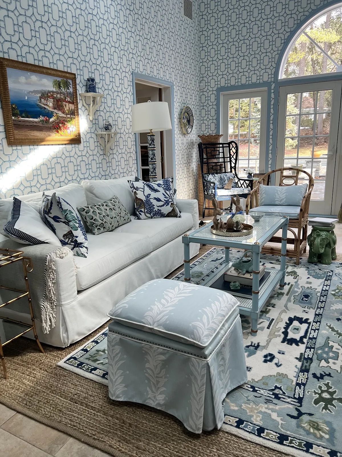 Living room with white sofa, glass coffee table, patterned rug, large windows, and light blue wallpaper.