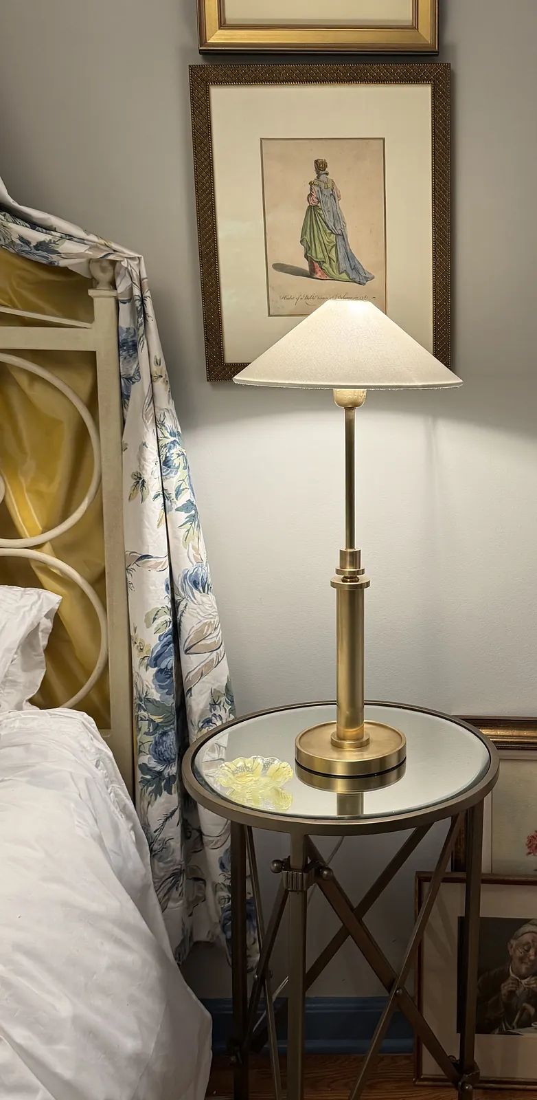 Bedroom with canopy bed, floral textile, glass-top side table, table lamp, and framed artwork.