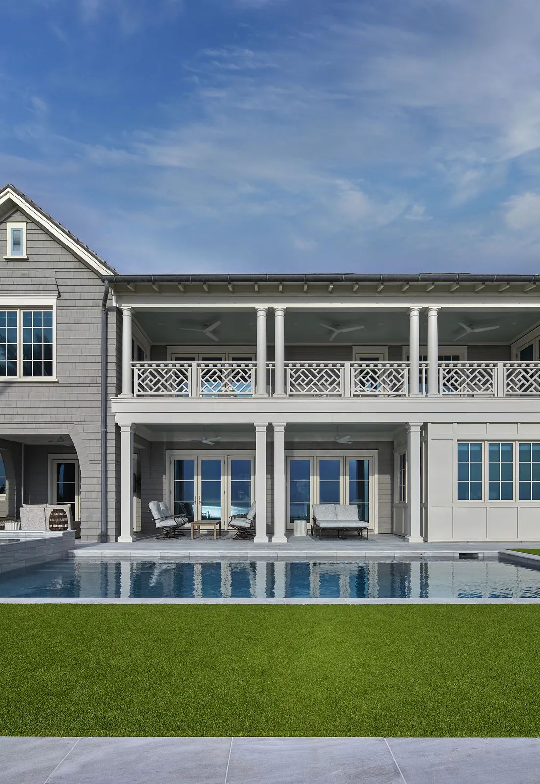 Exterior rear view with swimming pool, patio, lounge chairs, and a house with large windows and balcony.