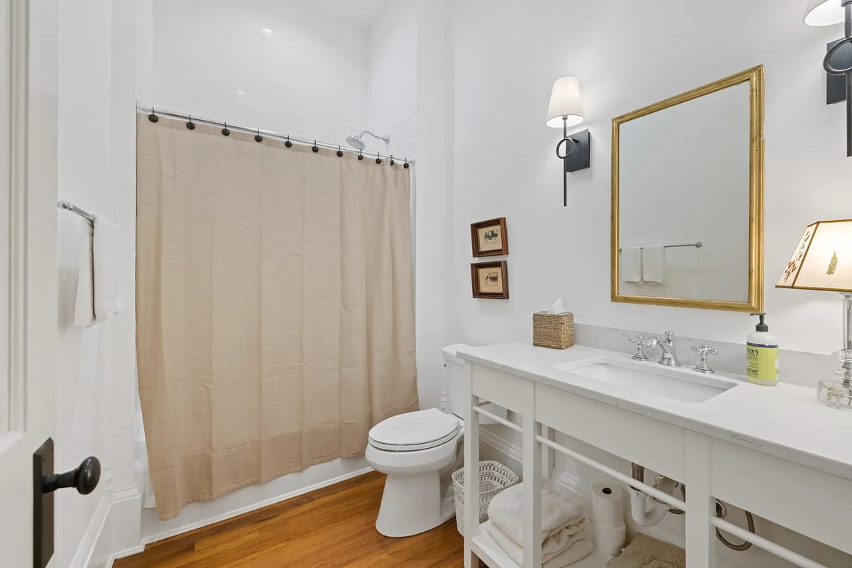 Bathroom with white vanity, marble countertop, beige shower curtain, and white toilet.
