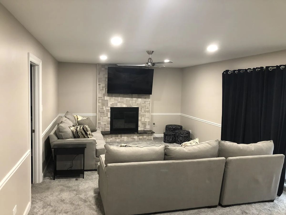 Living room with gray sectional sofa, black side table, television, stone fireplace, and black curtains.