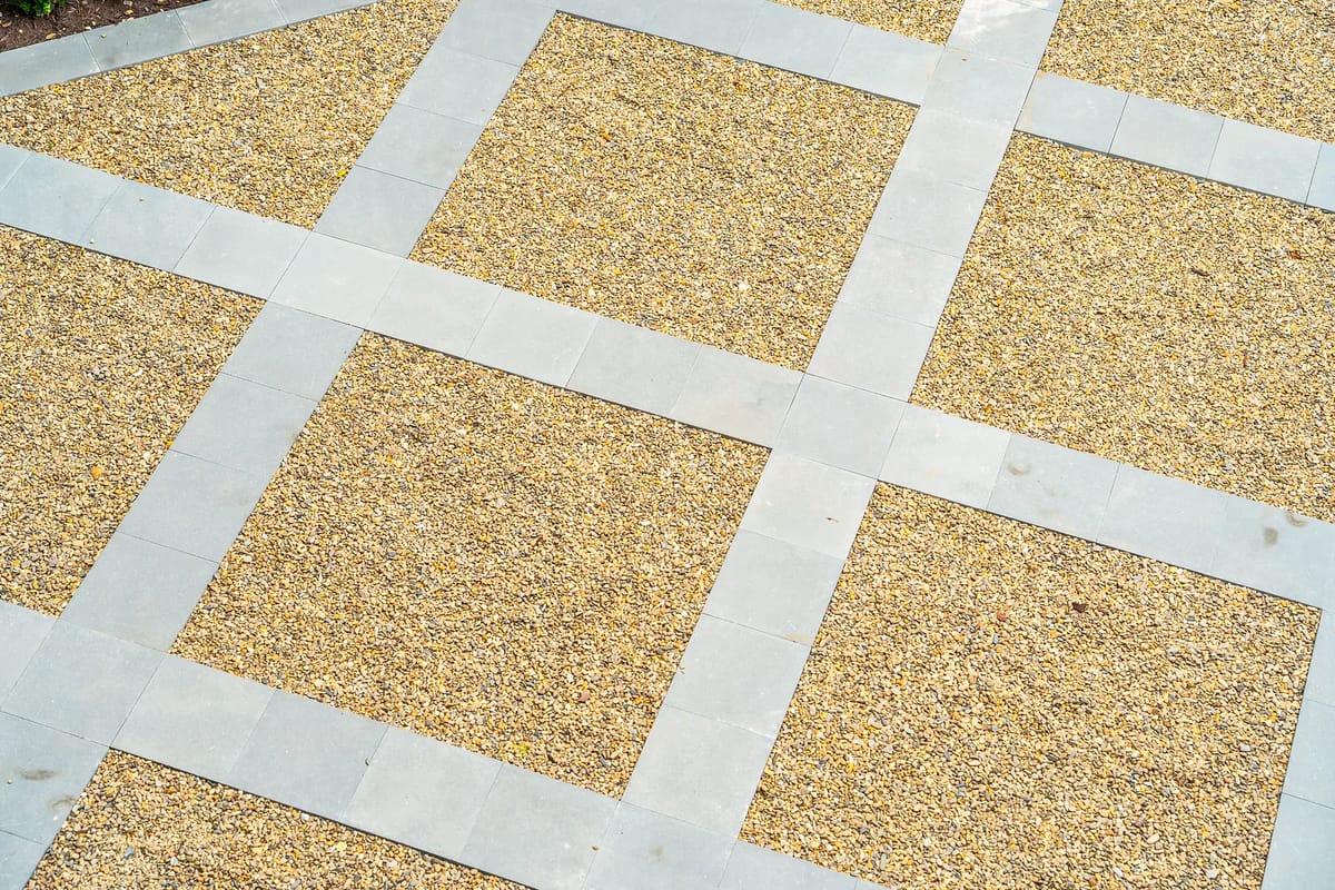 Garden area with gravel pathways bordered by stone slabs in a grid pattern.