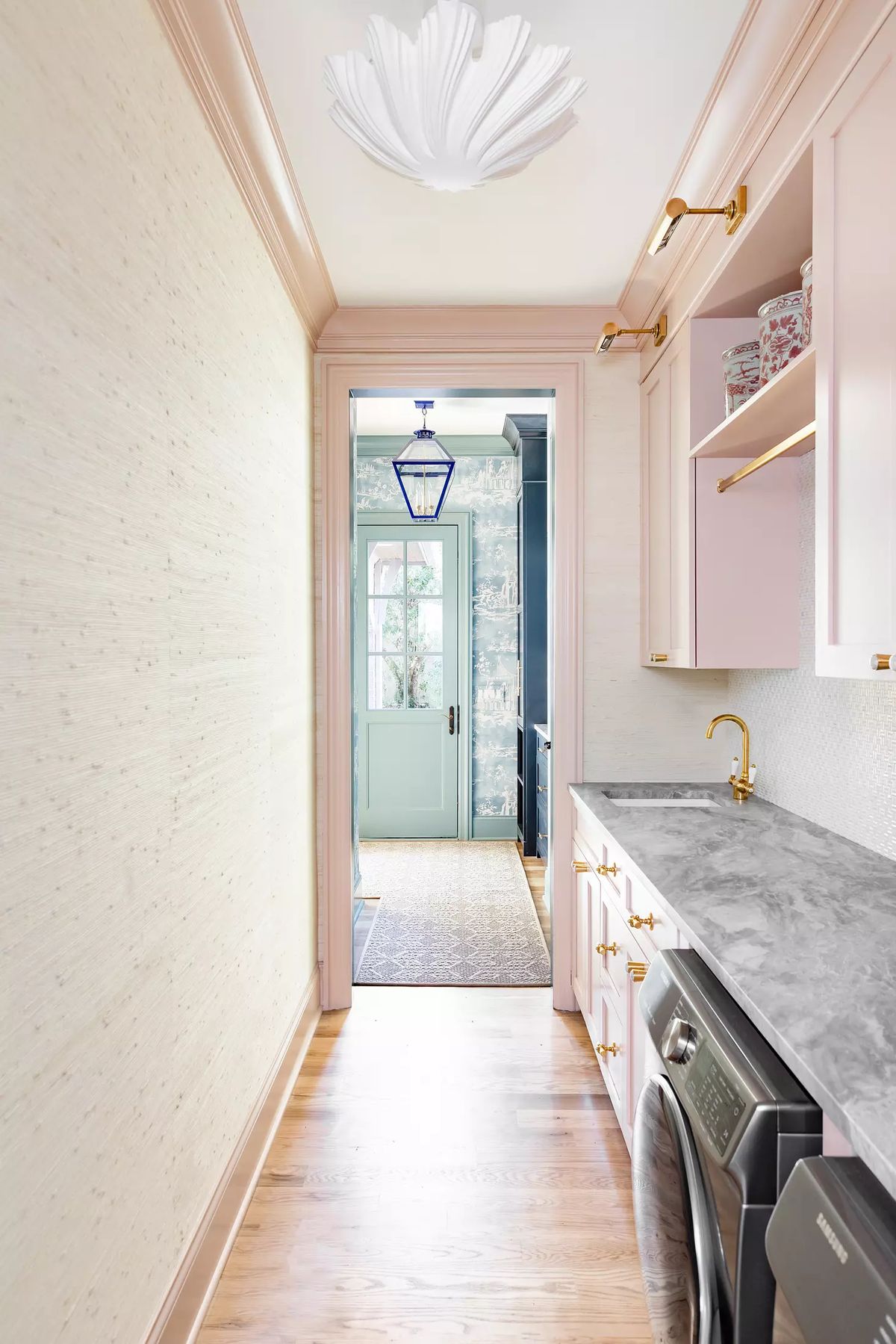 Laundry room with grey countertop, washing machine, pink cabinetry, and textured walls leading to an entrance.