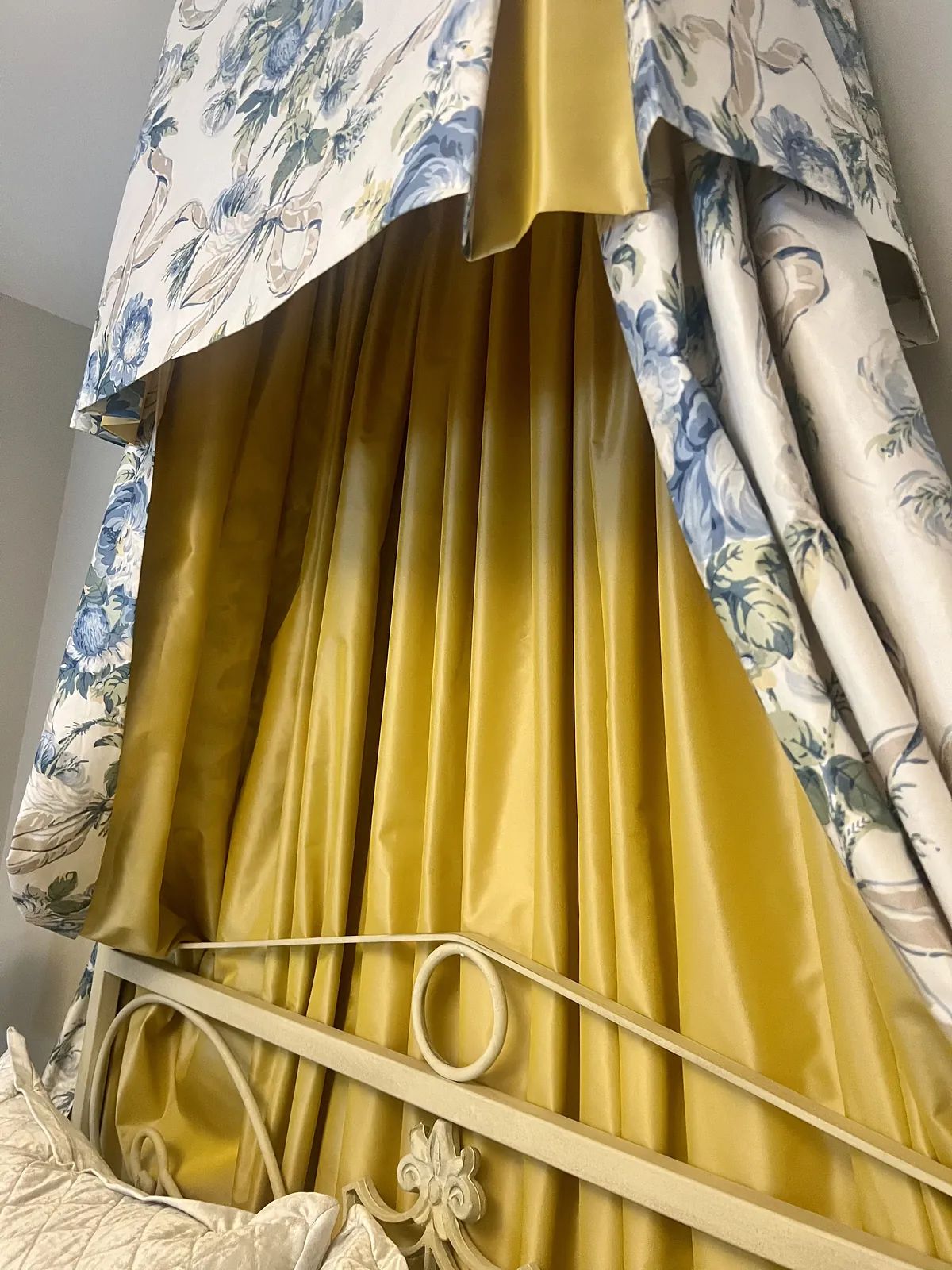 Bedroom with floral valance, yellow satin drapes, and ornate metallic headboard.