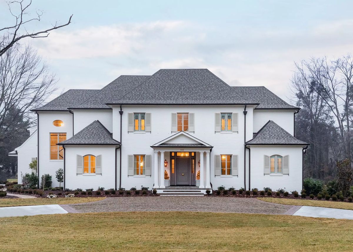 Two-story white house with gray roof, multiple windows, front porch, and landscaped yard