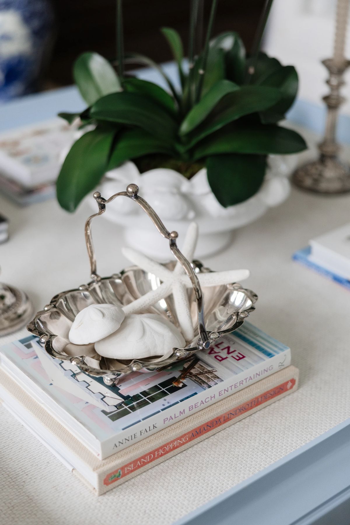 Tabletop arrangement with silver basket, starfish, books, and an orchid plant.