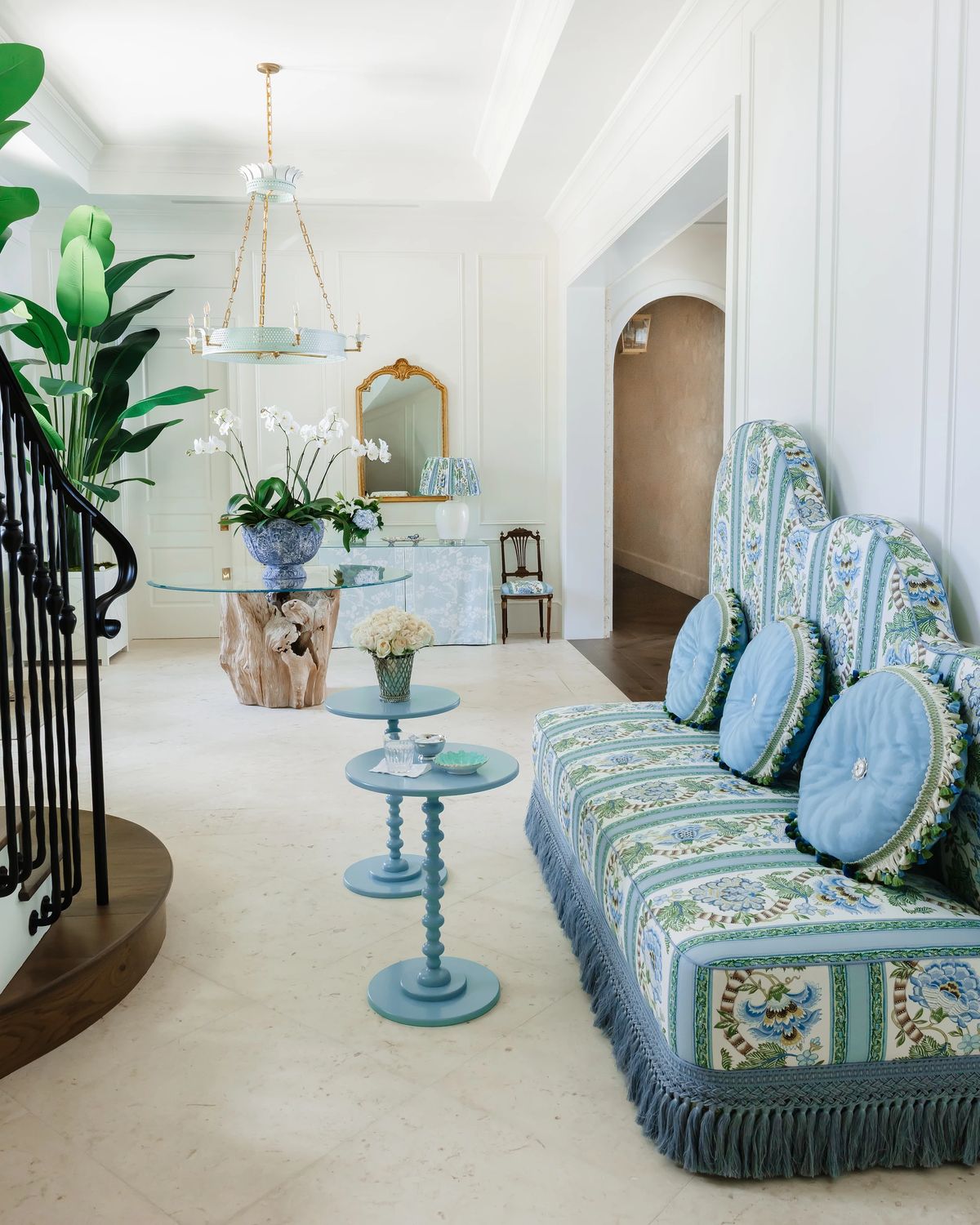 Foyer with patterned settee, blue side tables, chandelier, plants, and decorative mirror.