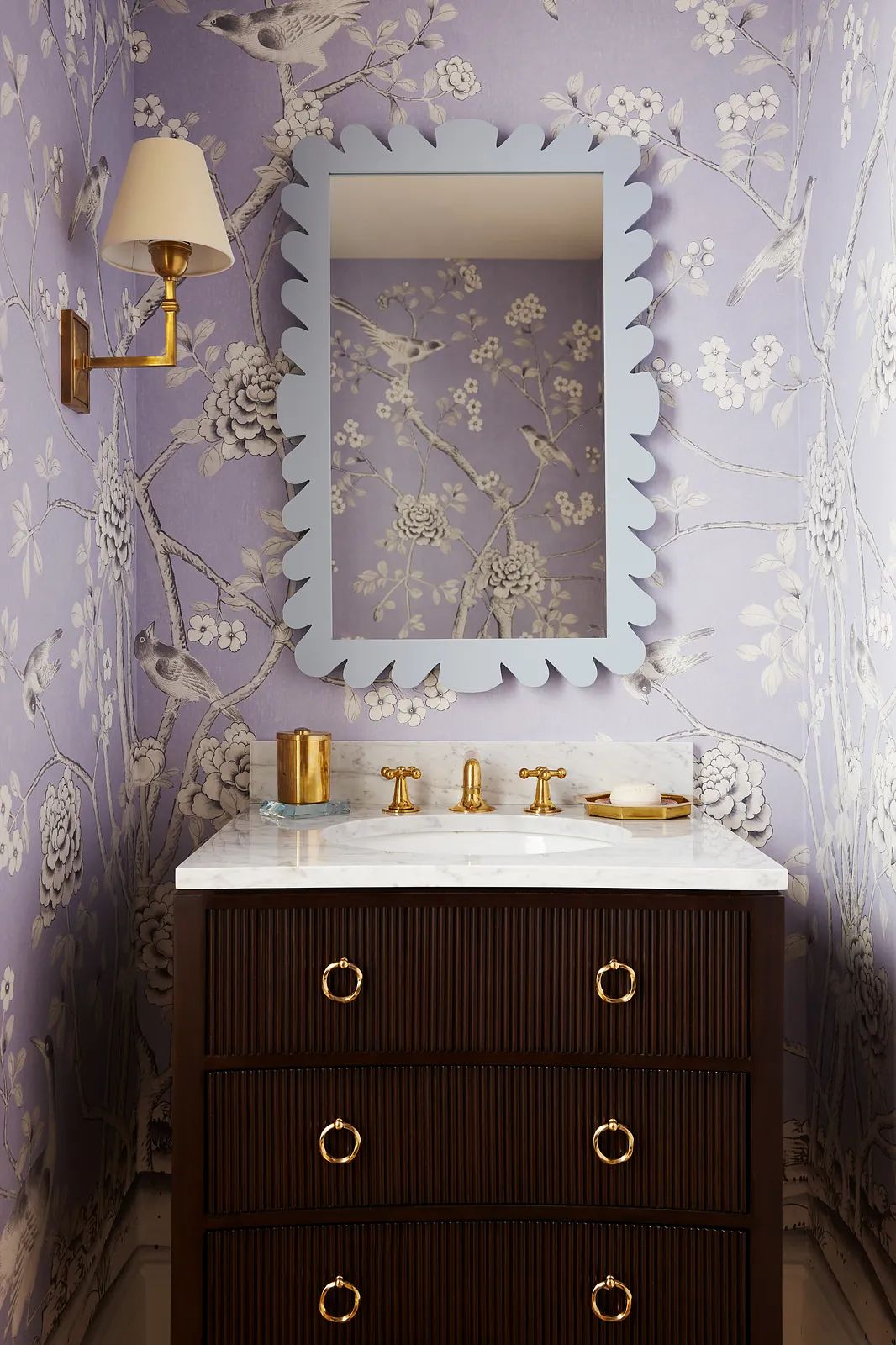 Bathroom with dark wood vanity, marble countertop, floral wallpaper, and wall sconce.