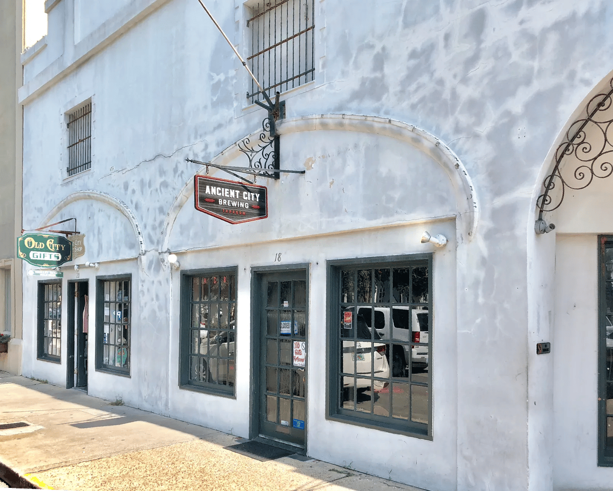 Exterior front of a building with white plaster, dark windows, and sign for Ancient City Brewing.