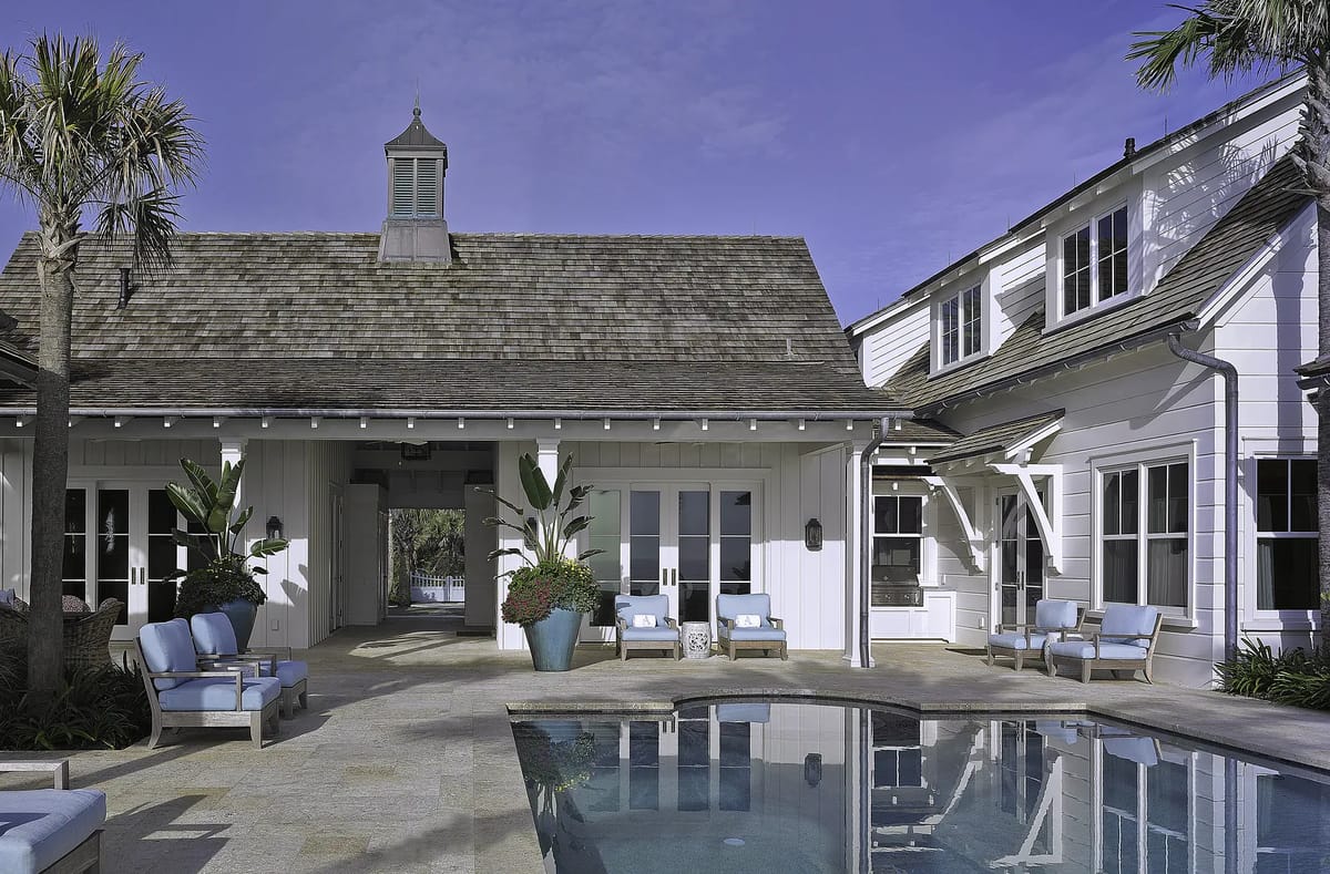 Exterior rear area with swimming pool, blue lounge chairs, planters, and white house with gabled roof.