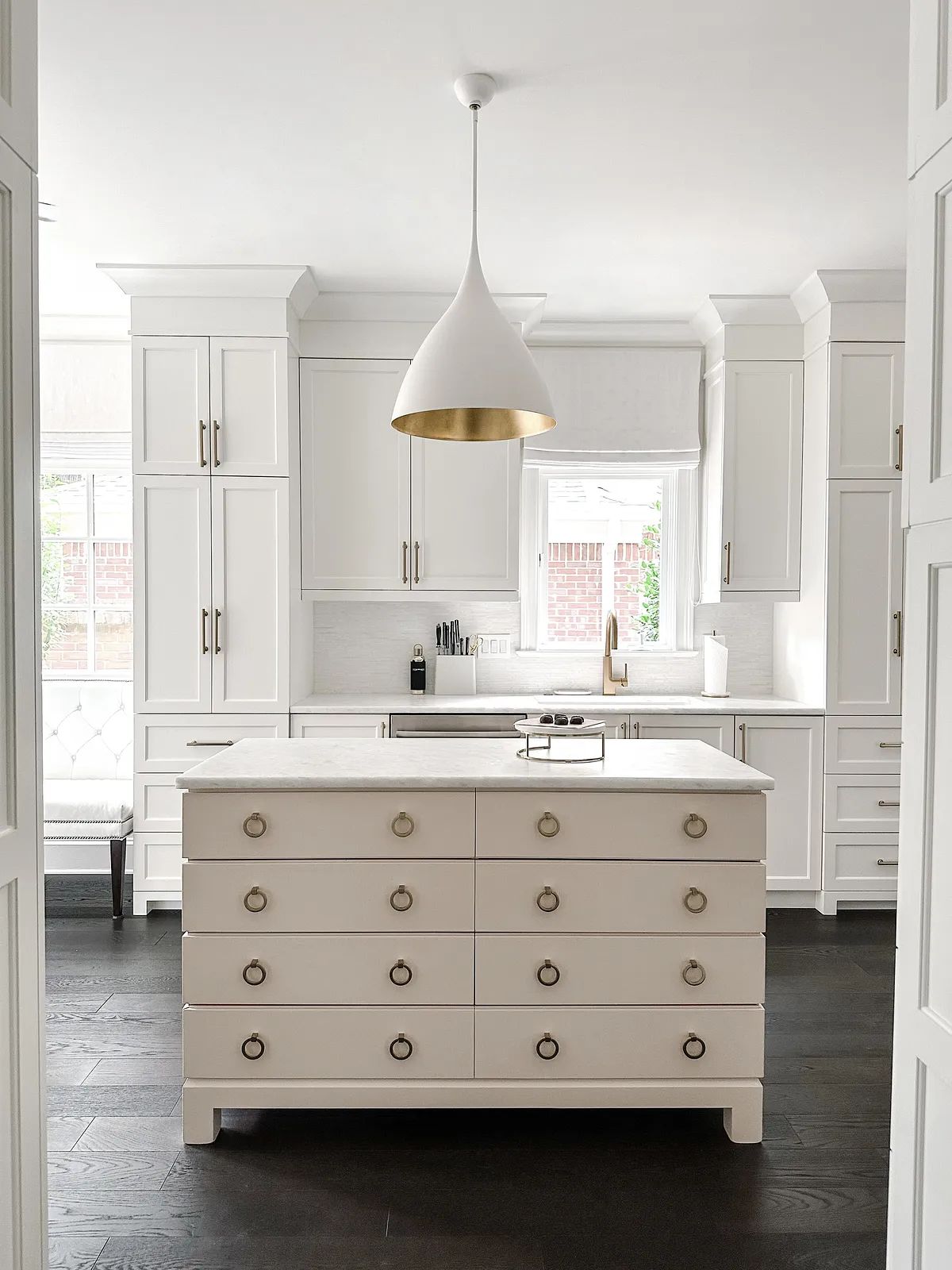 Kitchen with white cabinetry, central island, marble countertop, gold pendant light, and a gray chair against the wall.