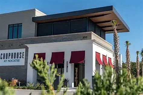 Exterior front view of a restaurant with red awnings, large windows, and gray brick facade.
