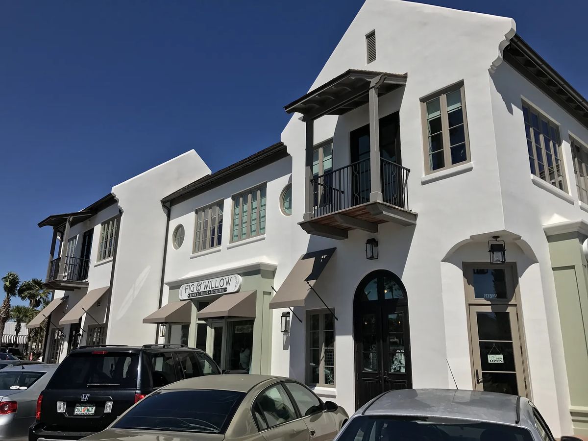 Exterior facade of a commercial building with white stucco, large windows, balcony, and signage.