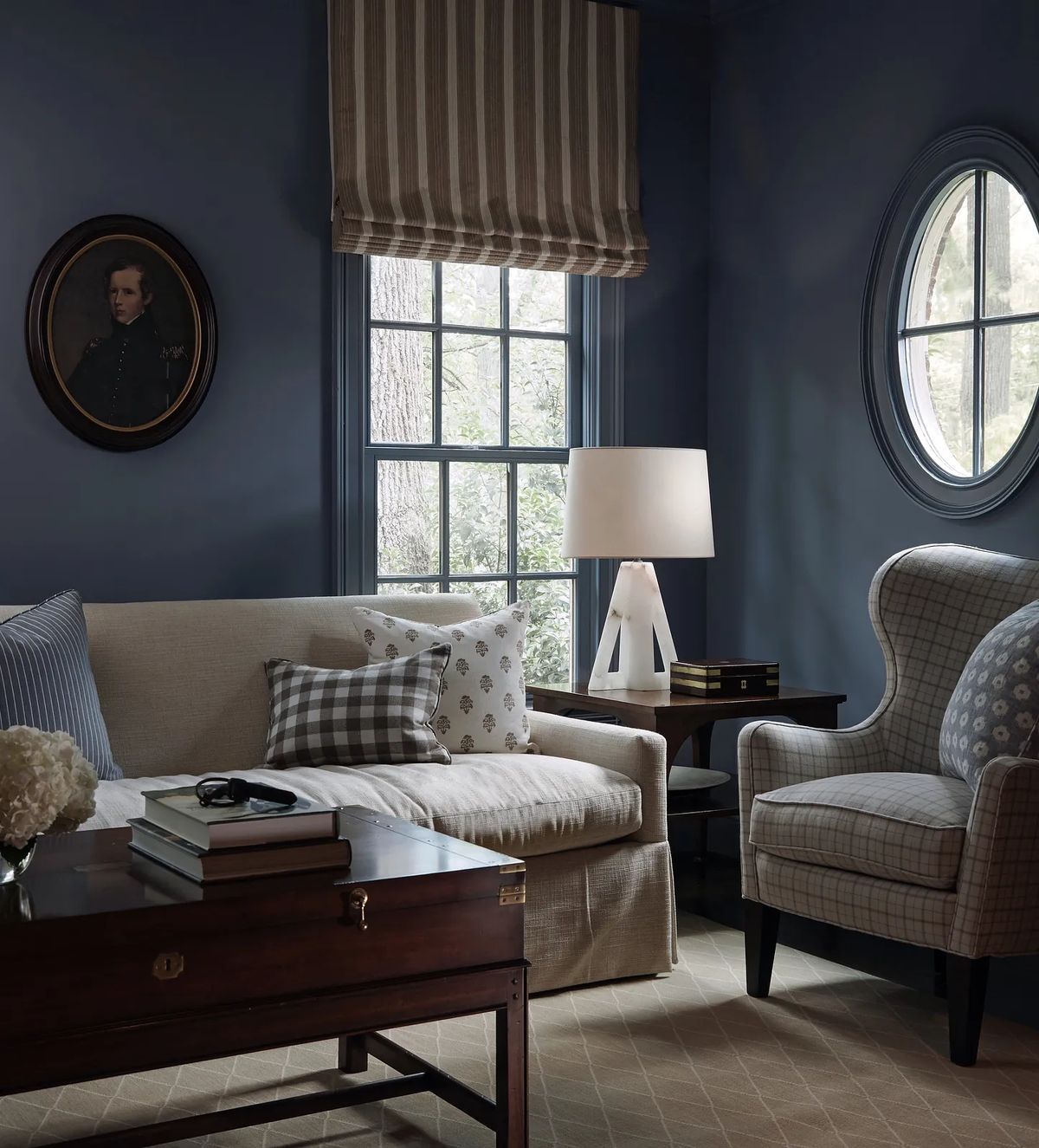 Living room with beige sofa, coffee table, checkered pillow, upholstered armchair, and blue walls with windows