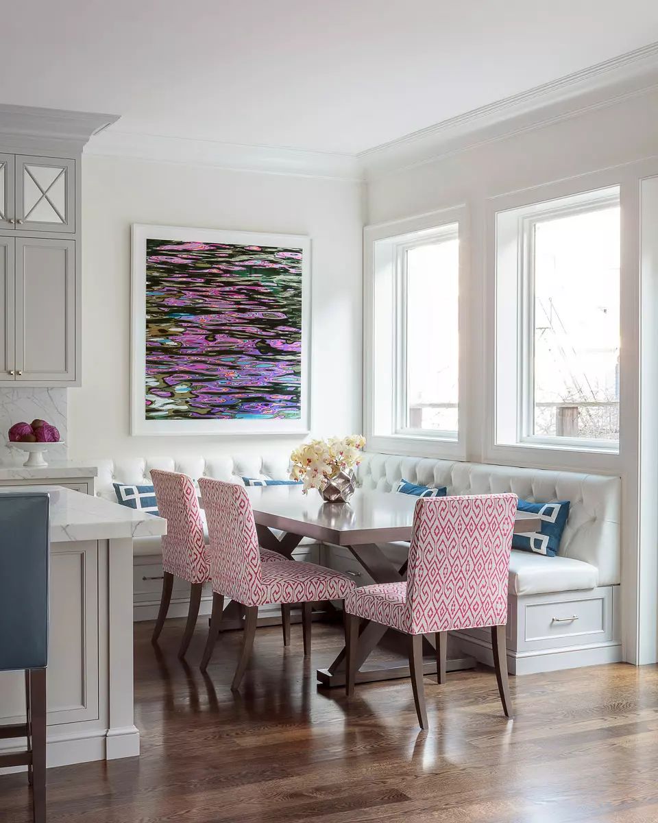 Dining room with corner banquette, table, pink chairs, artwork, and large windows for natural light