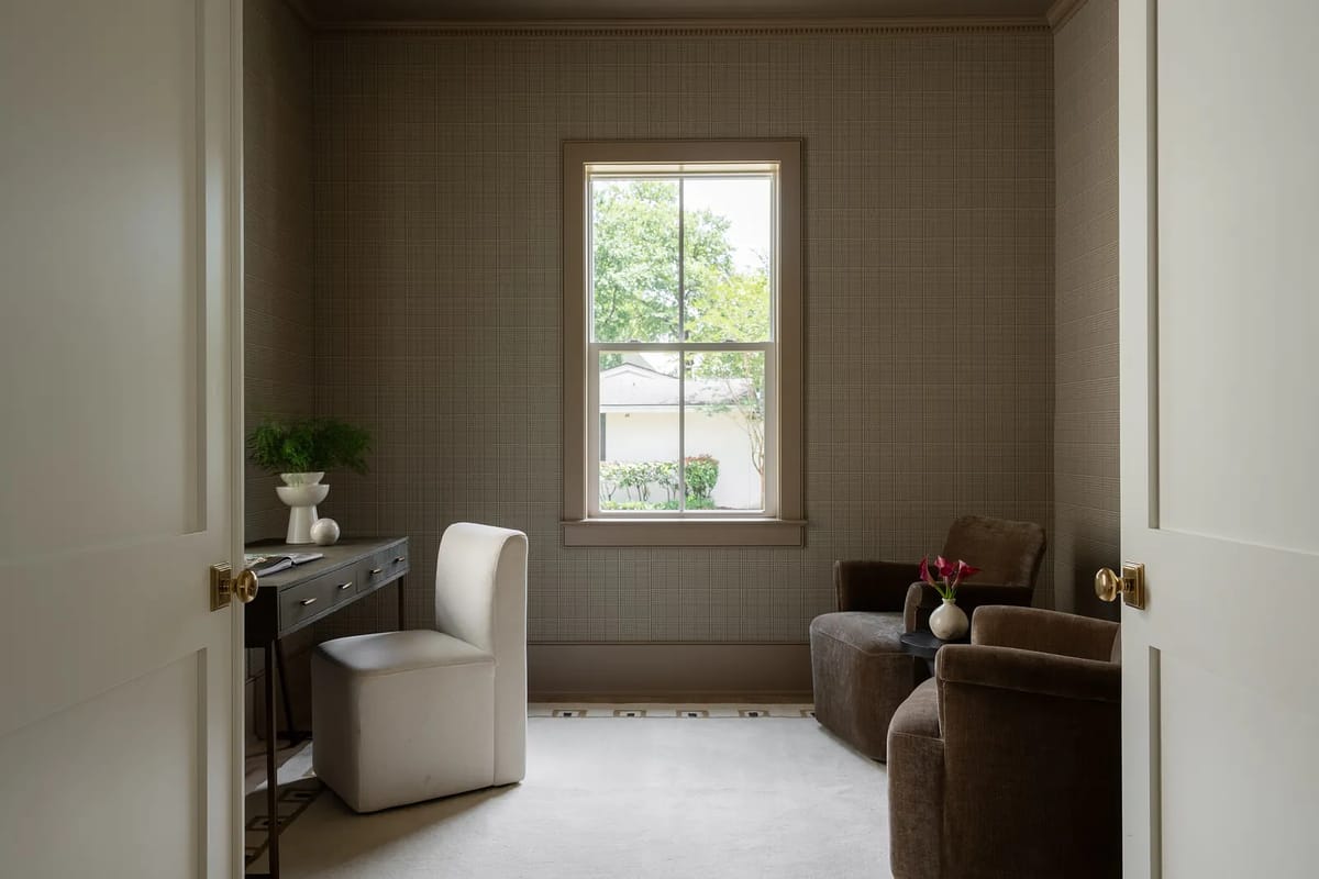 Office with desk, upholstered chair, brown armchair, window, and grid-patterned wallpaper.