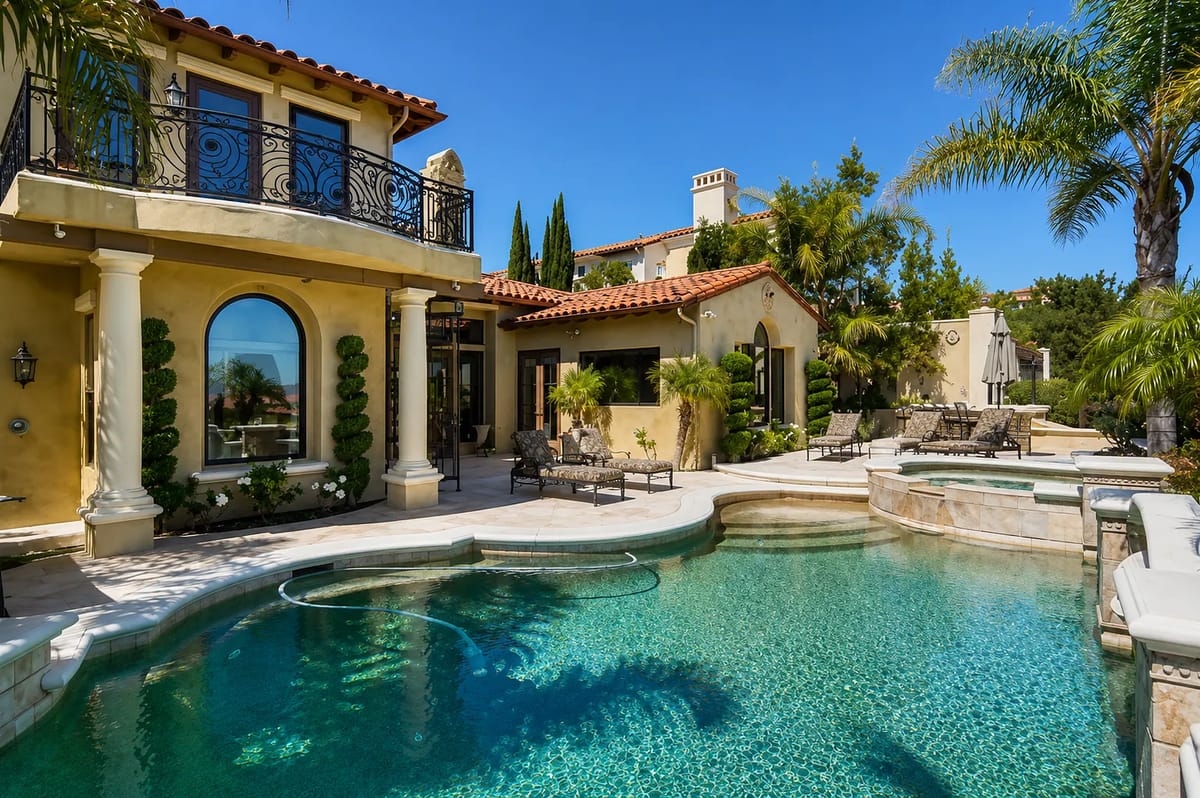 Exterior rear view with swimming pool, outdoor seating, stone walls, and palm trees.