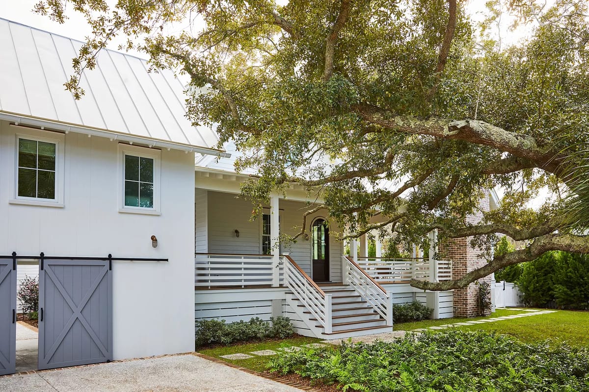Exterior front of a house with metal roof, white siding, porch, and large oak tree.