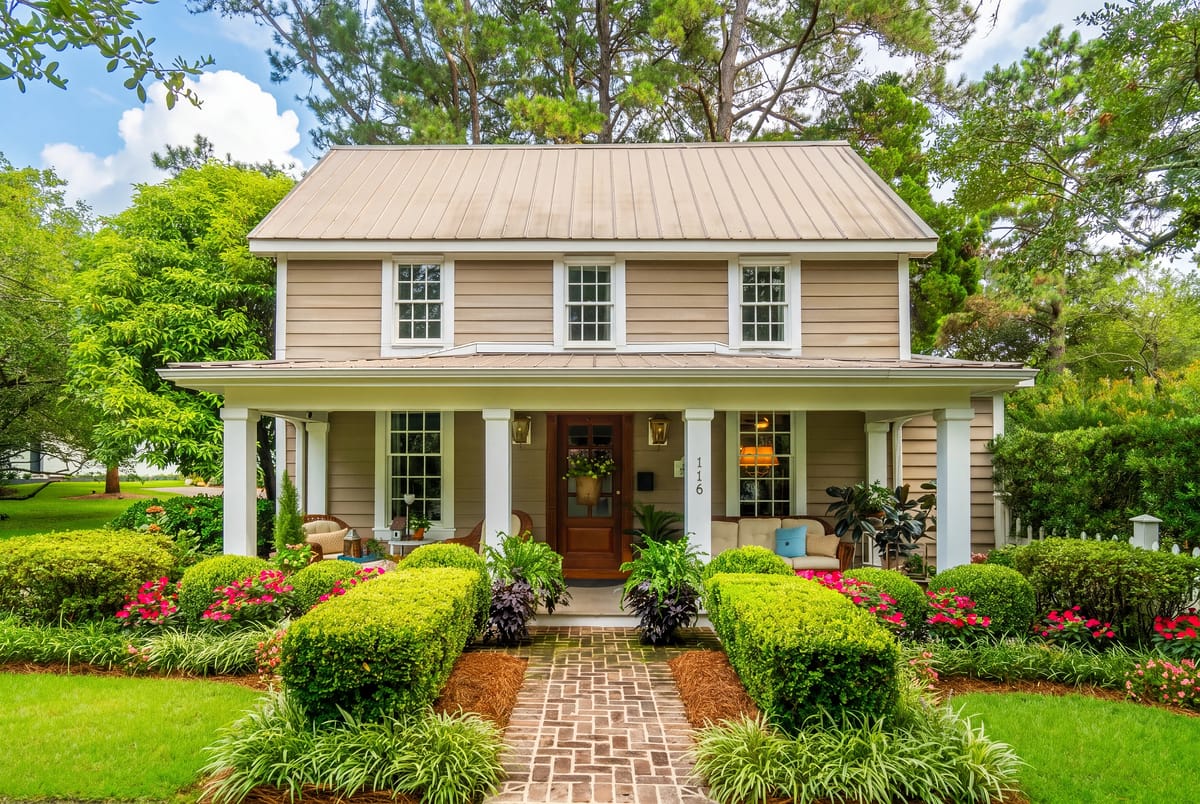 Exterior front of a two-story house with beige siding, white trim, brick pathway, and landscaped garden.