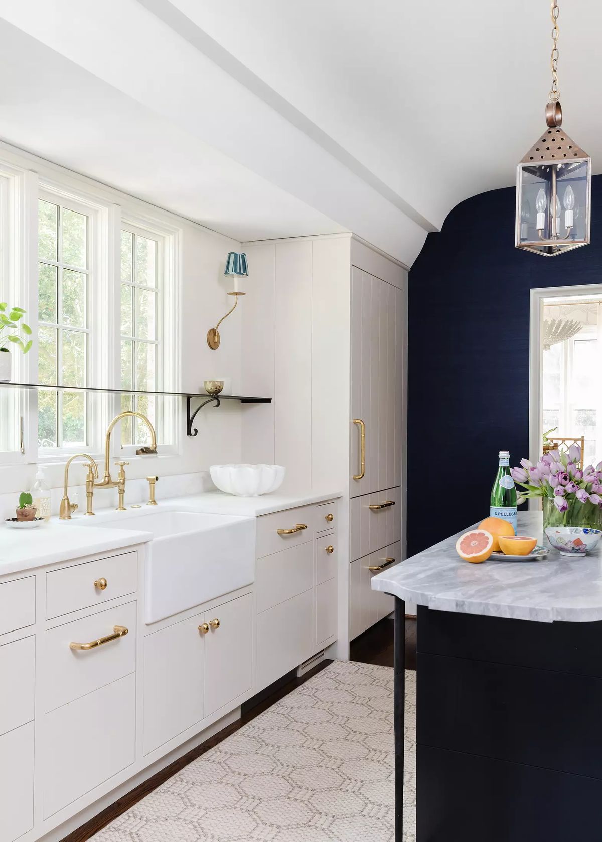 Kitchen with farmhouse sink, brass faucets, cabinetry, marble countertop, black island, and large windows