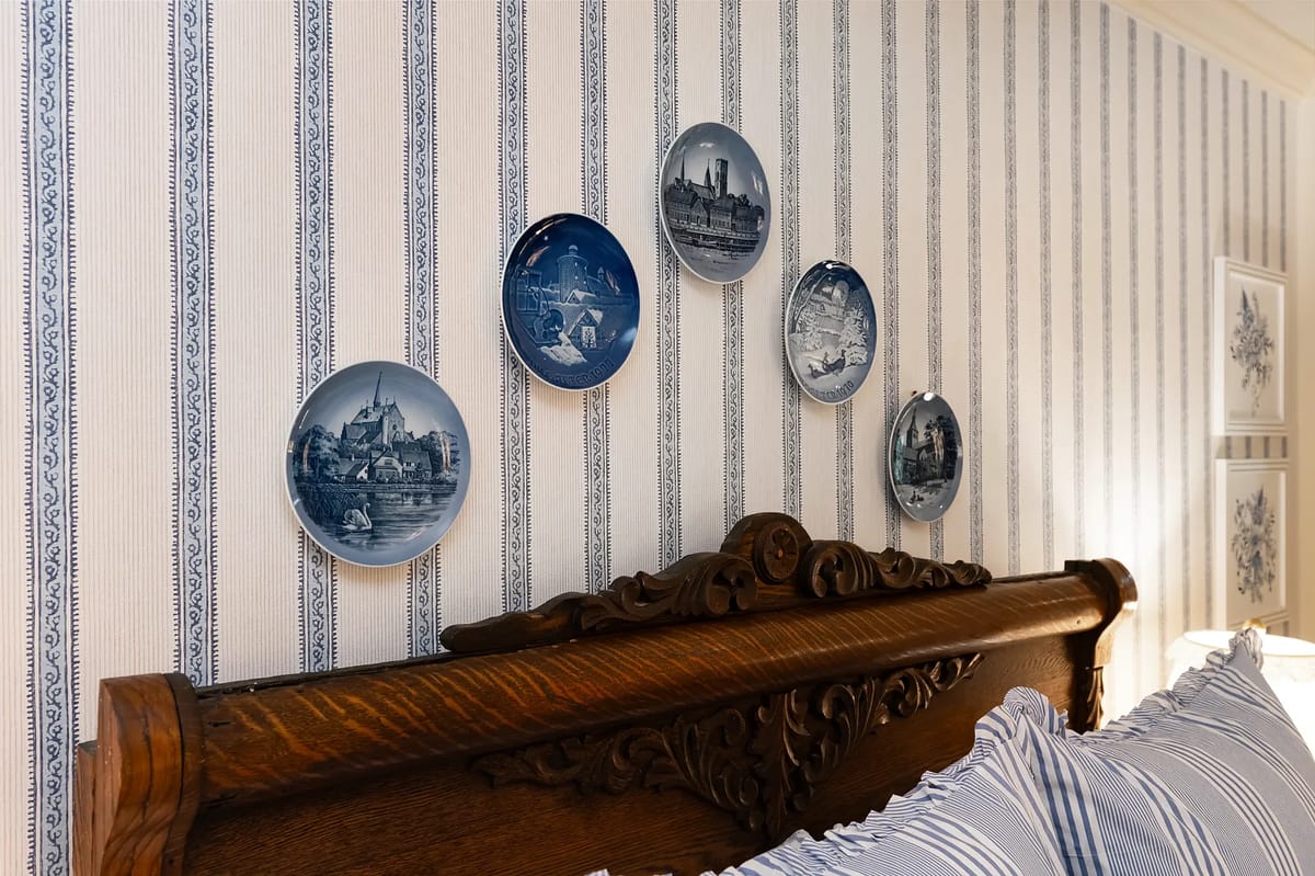 Bedroom with wooden headboard, striped bedding, and decorative landscape plates on striped wallpaper
