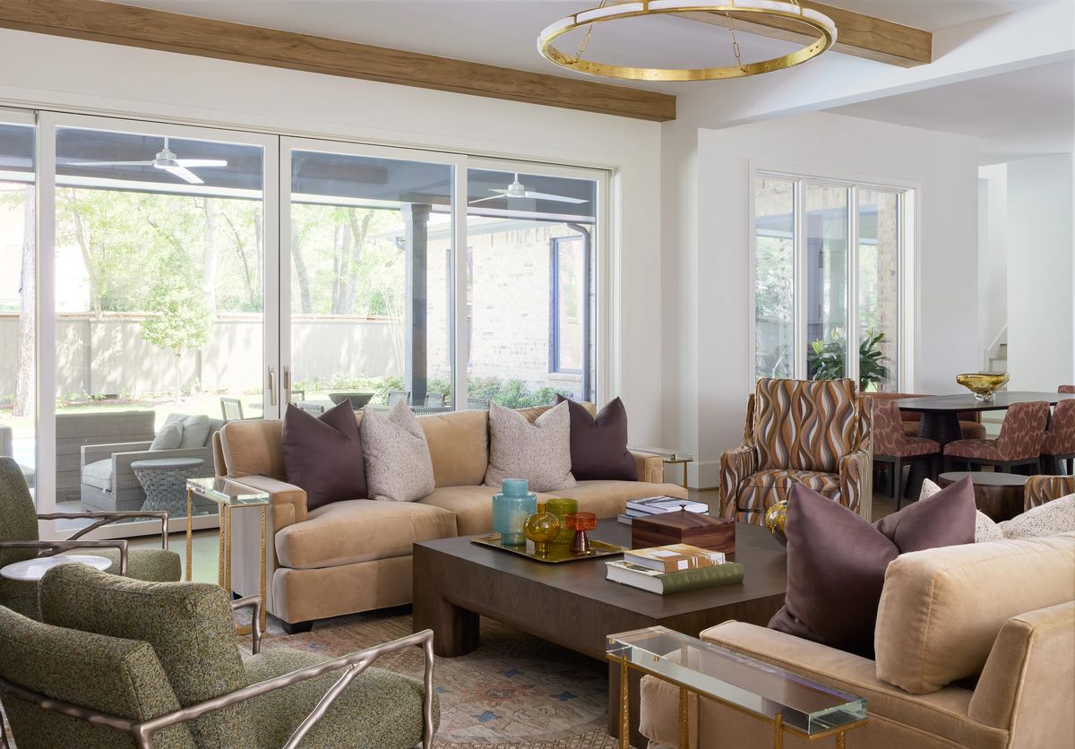Living room with beige sofas, green armchairs, wood coffee table, area rug, and large windows overlooking the garden.