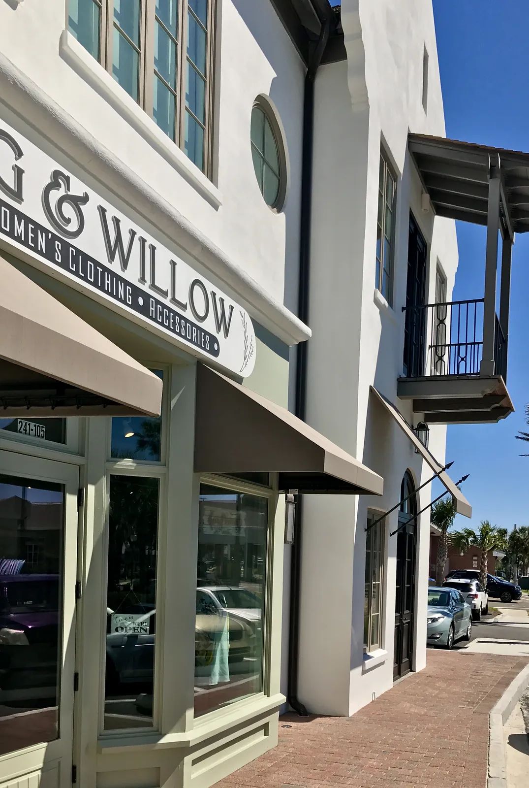 Exterior front of a retail store with window display, sign, awning, and balcony.