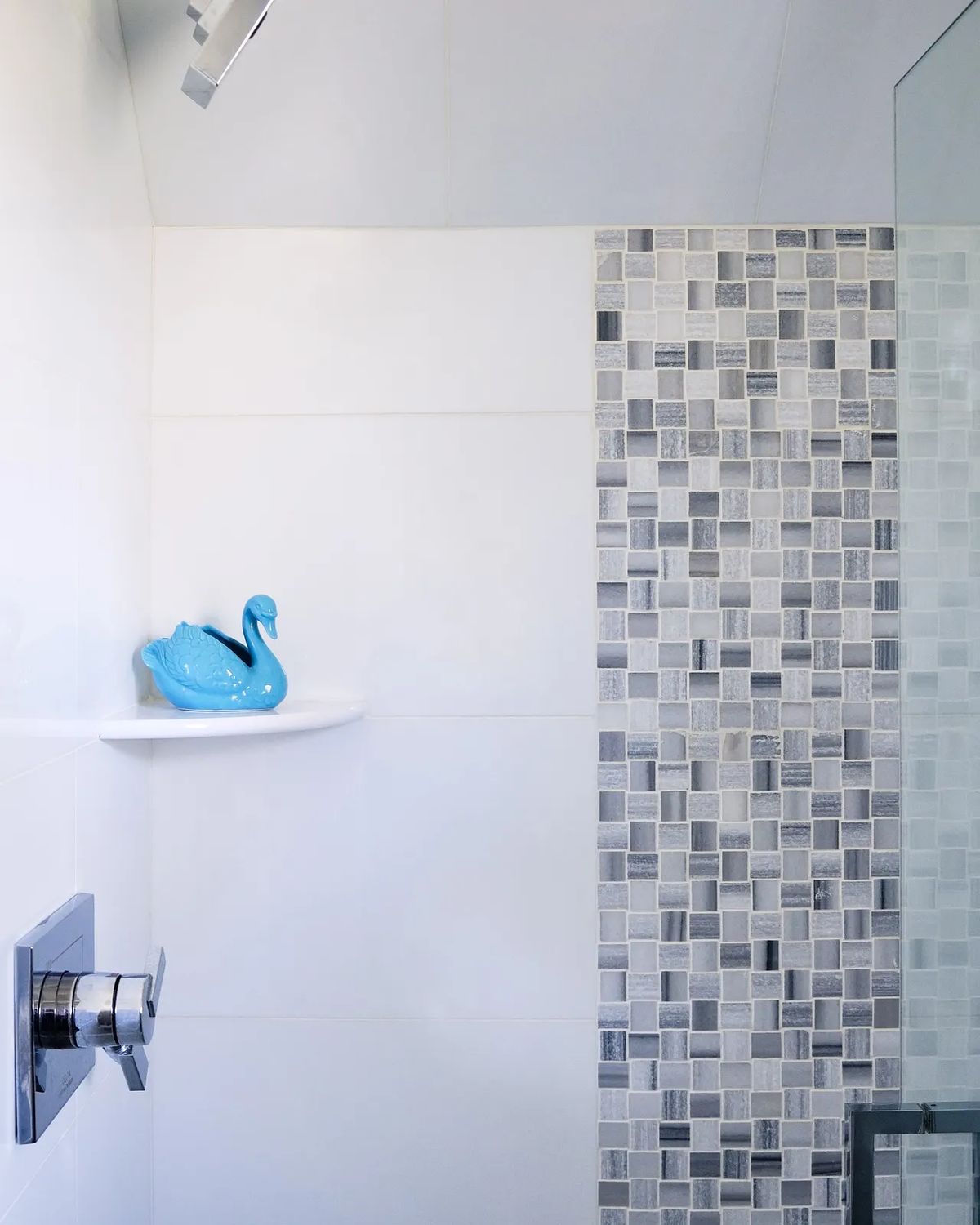 Bathroom with glass shower, mosaic tile wall, wall-mounted faucet, and blue ceramic swan decor.
