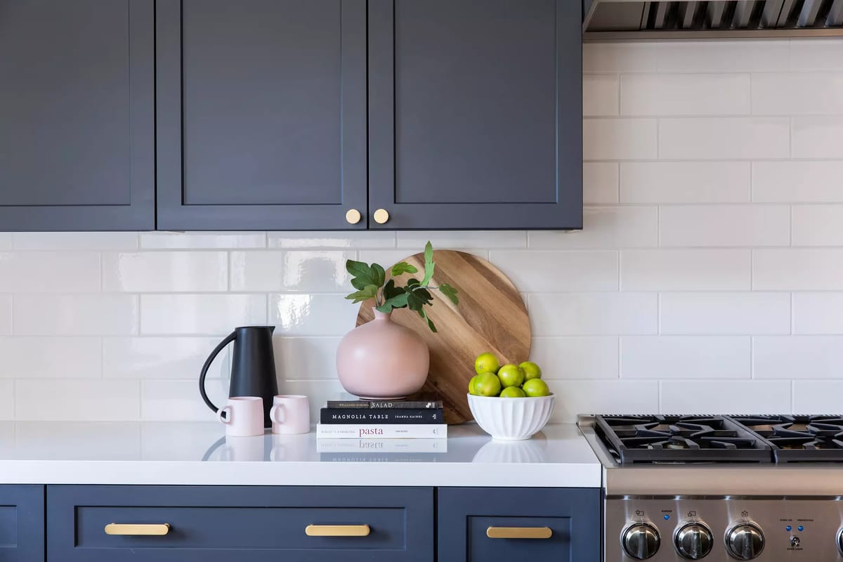 Kitchen with navy cabinets, white countertop, and decor including a black pitcher and green apples in a bowl.