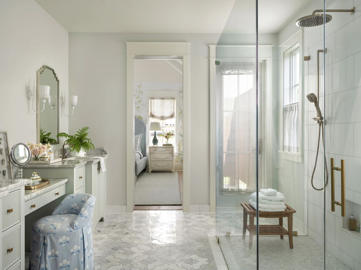 Bathroom with glass shower, marble floor, vanity, blue stool, and rolled towels.