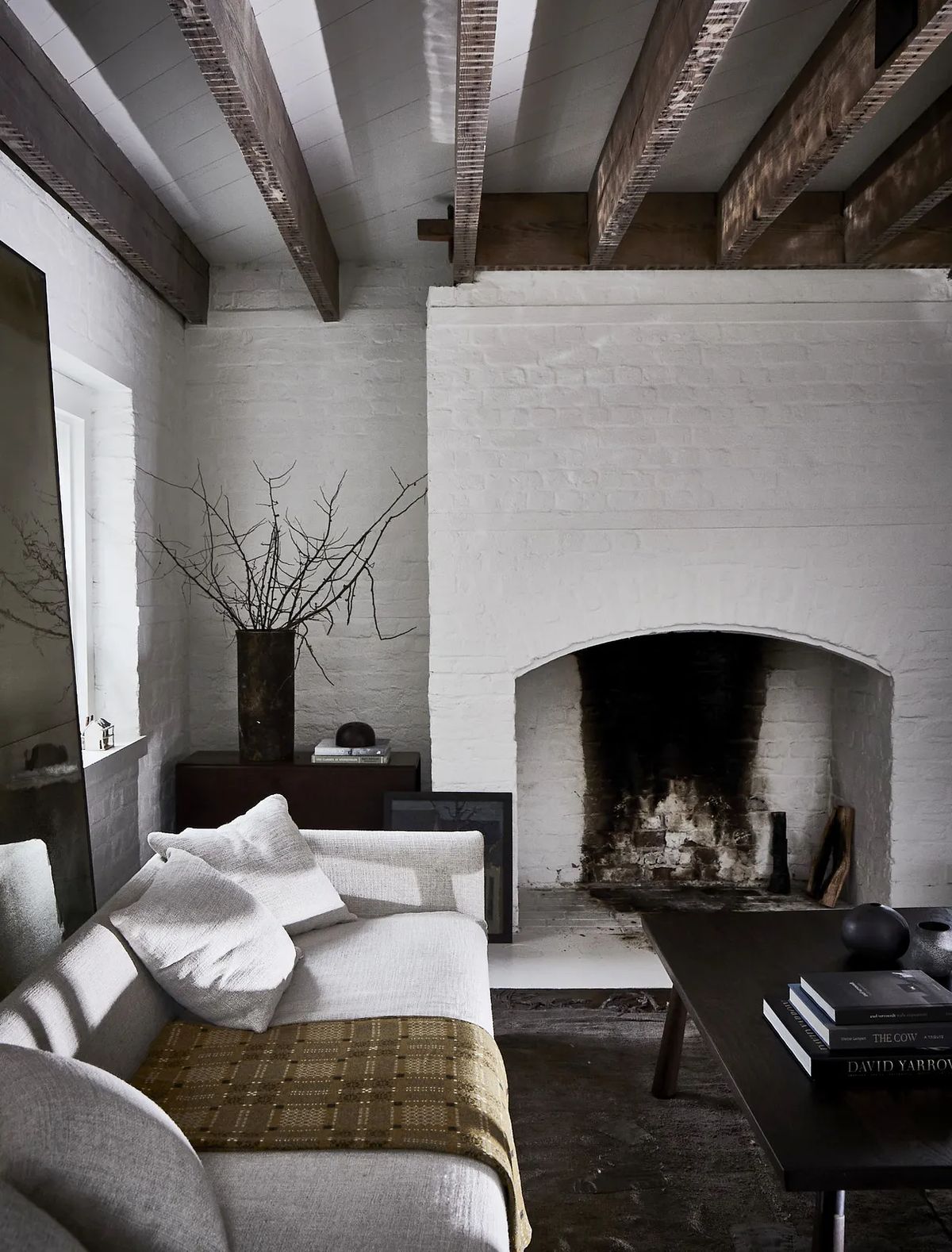 Living room with white brick fireplace, gray sofa, wood coffee table, wall mirror, and exposed beams.